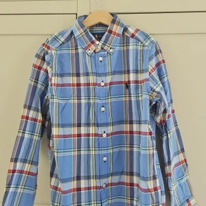 Rutig skjorta från Ralph Lauren blå - Snygg rutig skjorta från Ralph Lauren i blått med inslag av rött, grönt, gult och vitt. Skjortan har klassisk krage, långa ärmar och knappar framtill. Tillverkad i bomull med naturlig stretch för extra komfort. Perfekt för dig som gillar stilren och färgglad look.