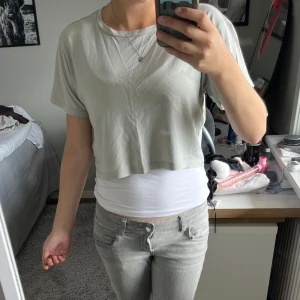 Ljusgrå croppad t-shirt från 157 - Enkel och stilren ljusgrå croppad t-shirt från 157. T-shirten har rund halsringning, korta ärmar och är tillverkad i 100% bomull. Har även ett litet hål som man ser på andra och sista bilden.Perfekt för en chill och avslappnad look.