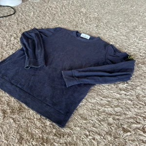 Äkta Mörkblå Stone Island sweatshirt - Säljer en mörkblå sweatshirt från Stone Island med klassisk rund hals och lång ärm. Tröjan har den ikoniska loggan på vänster ärm och är tillverkad i mjuk bomull. Perfekt för dig som gillar stilrena och snygga plagg med streetkänsla.