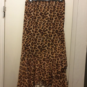 Långkjol från Nelly i leopad - Snygg långkjol från NLY Trend med leopardmönster i bruna och svarta toner. Kjolen har volangdetalj nertill och är tillverkad i ett lätt, flowy material. Storlek M. Aldrig använd då jag tycker den är för lång för min smak:)