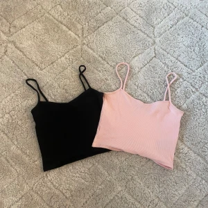 2-pack Monki croppade linnen XXS - Två croppade linnen från Monki i storlek XXS. Ena är svart och den andra ljusrosa, båda med smala axelband och ribbad struktur. Perfekta för sommaren och lätta att matcha med jeans eller shorts.