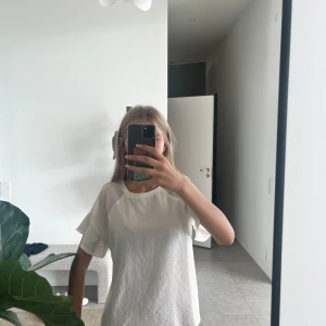 Vit blus med volangärm från Object - Säljer en söt vit blus från Object i storlek 34. Blusen har korta volangärmar och rund halsringning. Materialet är lätt och har en diskret struktur som ger en fräsch känsla. Perfekt att styla med jeans eller kjol för en clean look.