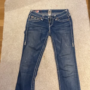 True Religion Billy Super T jeans blå - Säljer ett par blå True Religion jeans med vita kontrastsömmar och snygga detaljerade bakfickor. Klassisk femficksmodell med låg midja och raka ben. 