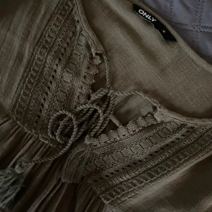 Grön långklänning från ONLY med snörning - Säljer en grön långklänning från ONLY i boho-stil. Klänningen har långa ärmar, snygga virkade detaljer upptill och snörning med tofsar vid halsen. Luftig och skön modell som passar perfekt till varmare dagar.