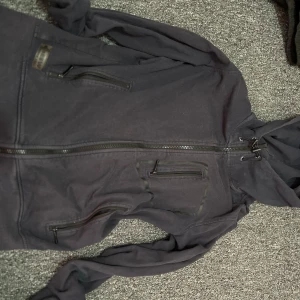 Svart vindjacka från South West - Svart jacka från South West med huva och dragsko. Jackan har flera praktiska fickor med dragkedja och en stilren design. Tillverkad i ett slitstarkt material som passar perfekt för blåsiga dagar. Snygg och funktionell jacka för dig som gillar enkel stil.