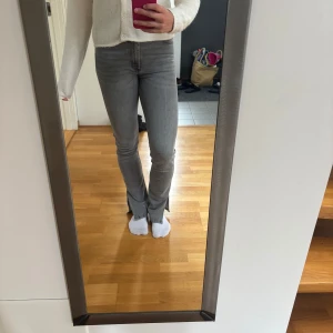 Grå jeans med slits nertill - Säljer ett par grå jeans med raka ben och snygga slitsar nertill. Jeansen har medelhög midja och klassisk femficksdesign. De är i stretchigt denim som sitter tajt upptill och släpper lite vid vaden. 