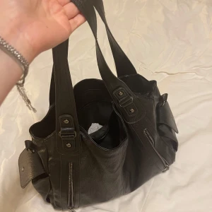 Svart axelväska i skinn med dragkedjor - Rymlig svart axelväska i skinn med flera fack och dragkedjor. Väskan har breda axelband, snygga metalldetaljer och praktiska ytterfickor med dragkjedja. Perfekt för dig som vill ha plats för allt du behöver under skolan eller för vardags små tecken på användning i banden .diskuterbart pris🩷