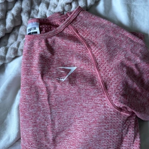 Rosa Gymshark t-shirt  - Så snygg gymtisha från gymshark! Superskönt material och en ganska tight fit som formar kroppen så snyggt 🩷 ganska använd men fortfarande väldigt bra skick! Säljer fler produkter från gymshark på min profil! 