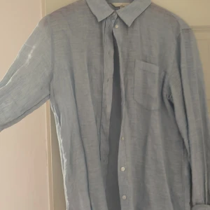 Ljusblå linneskjorta med ficka från HM - Snygg ljusblå skjorta i linne med klassisk krage och bröstficka. Skjortan har långa ärmar och knäppning framtill. Perfekt för en avslappnad och stilren look.