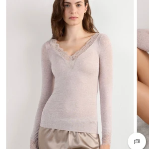 Beige långärmad topp med spetsdetaljer - Supersöt beige långärmad topp med v-ringning och fina spetsdetaljer vid halsringning och ärmslut. Sitter tight och har en feminin vibe, perfekt att styla med både jeans och kjol. Mjuk och stretchig känsla, passar dig som gillar en enkel men ändå elegant look. Finns en del hål i tröjan som jag skickar bild på privat om någon är intresserad 