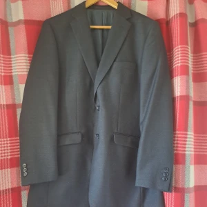Mörkgrå kavaj från Batistini - Stilren mörkgrå kavaj från Batistini med klassisk passform. Kavajen har två framfickor med lock, bröstficka och tre knappar vid ärmslut. Perfekt för formella tillfällen.