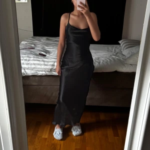 Svart långklänning med smala axelband - Klänning från asos, använt den endast två gånger på tidigare bröllop för något år sen, bra skick. Är 167cm, midja och bröst storlek går att justera med hjälp av banden på ryggen.