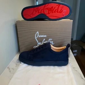 Mörkblåa  sneakers från Christian Louboutin - Säljer ett par svarta sneakers från Christian Louboutin med klassisk röd sula och ovandel i mocka. Skorna har rund tå, svarta skosnören och beige innersula med logotyp. Perfekta för dig som vill ha en stilren och lyxig look.