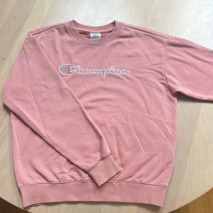 Rosa sweatshirt från Champion - Säljer en rosa sweatshirt från Champion med broderad logga framtill. Tröjan har rund halsringning och långa ärmar. Perfekt för en avslappnad och sportig stil. Klassisk passform och mjukt material. 