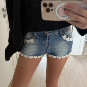 Blå lågmidjade jeansshorts med blommig spetskant - Supersöta blå jeansshorts med låg midja, vit blommig spetskant längs fickor och benslut💞💞💞💞 