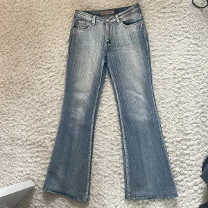 Blåa lågmidjade bootcut jeans från Bannyger - Säljer ett par blå bootcut jeans från Bannyger med slitningar och ljus tvätt. Jeansen har fem fickor, nitar på bakfickorna och klassisk knappgylf. Perfekta för dig som gillar en retro vibe och vill ha ett par lågmidjade jeans 