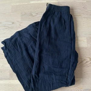 Svarta vida linnebyxor - Säljer ett par svarta, luftiga linnebyxor med resår i midjan. Byxorna har en avslappnad och vid passform, perfekta för varma dagar eller en chill stil. Materialet är lätt och har en skrynklig struktur.