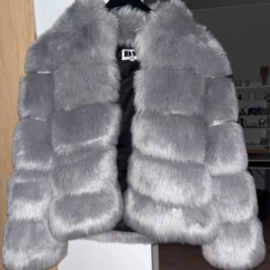 Grå pälsjacka - Säljer en fluffig och lyxig grå pälsjacka med breda paneler och krage. Jackan är långärmad och har en riktigt mjuk och voluminös look. Perfekt för dig som vill sticka ut och hålla dig varm under kyliga dagar.Nästan oanvänd!!!! 