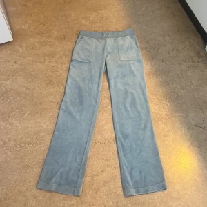 Ljusblå mjukisbyxor från Juicy Couture - Säljer ett par ljusblå mjukisbyxor från Juicy Couture med bred resår i midjan och fickor både fram och bak. Byxorna har raka ben och är gjorda i ett mjukt, syntetiskt material. Perfekta för en avslappnad stil, men om man ändå vill klä upp sig lite 