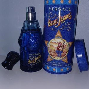 Versace Blue Jeans Man Eau de Toilette - Versace Blue Jeans Man är en parfym i en blå glasflaska med detaljerad design och gul text. Flaskan kommer i en rund, blå metallburk med westerninspirerat motiv och guldiga detaljer. Doften är fräsch och maskulin, perfekt för dig som gillar klassiska och ikoniska parfymer.