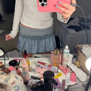 Blå jeanskjol med smock i midjan - Supersöt kort jeanskjol med smockad midja och lätt volang nedtill. Perfekt för en avslappnad och trendig look. Kjolen har en ljusblå tvätt och är enkel att matcha med olika toppar.