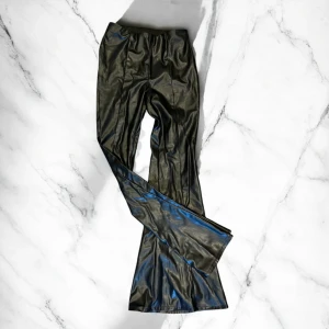 Svarta byxor i skinnimitation från Divided - Säljer ett par svarta byxor i skinnimitation från Divided. Byxorna är low waist och en tight passform med vida ben. Perfekta för dig som vill ha en edgy look med trendig känsla.