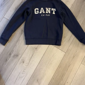Mörkblå sweatshirt från GANT - Säljer en klassisk mörkblå sweatshirt från GANT med vit broderad logga och texten 'Est. 1949' på bröstet. Tröjan har rund halsringning och långa ärmar. Perfekt för en avslappnad och stilren look.