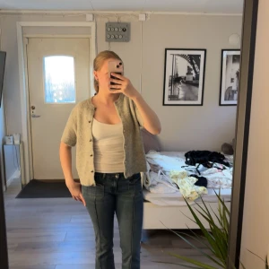 Ljusgrå stickad kofta från Gina Tricot - Supermjuk ljusgrå stickad kofta från Gina Tricot med korta ärmar och rund hals. Koftan har knappar framtill och ribbade kanter. Perfekt att slänga över ett linne eller t-shirt för en chill look.