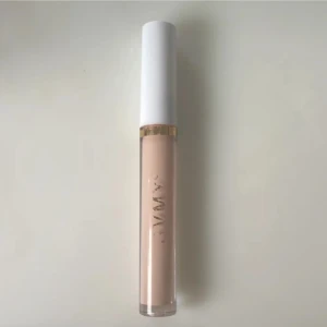 Flytande concealer med applikator - En flytande concealer i en ljus beige nyans. Kommer i en genomskinlig tub med vit kork och guldigt band. Applikatorn är vinklad för enkel applicering under ögonen eller på blemmor.