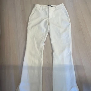 Vita kostymbyxor med bootcut - Säljer ett par vita kostymbyxor med bootcut och normal passform. Byxorna har fickor fram och stängs med dragkedja och knapp. Perfekta för en stilren look och passar till många olika outfits.
