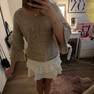 Beige stickad tröja med volang armar  - Mysig beige stickad tröja med v-ringning och volang, trekvartsärmar. 