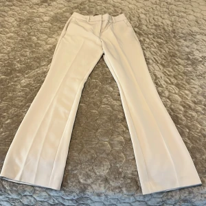 Vita kostymbyxor med bootcut - Säljer ett par stilrena vita kostymbyxor med bootcut-modell. Byxorna har medel hög midja och vida ben. Byxorna har ej använda. 