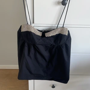 Svart linnetopp med strassdetaljer - Snygg svart linnetopp med tunna axelband och glittriga strassdetaljer längs bysten. Perfect till en utekväll!🤩aldrig använt