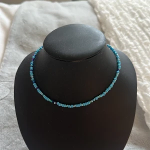 Blått pärlhalsband - Säljer ett halsband med små blå pärlor i olika nyanser. Halsbandet har en enkel och stilren design som passar perfekt till att ge din outfit lite extra färg.