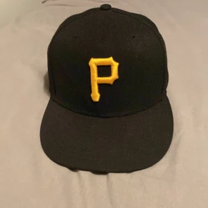 Svart keps från New Era med gul P-logga - Säljer en svart keps från New Era med en broderad gul P-logga framtill. Klassisk basebollmodell med MLB-logga baktill. Storlek 7 (55,8 cm). Perfekt för dig som skön och avslappnad stil. Ordinarie pris:499 Mitt pris:249. Använd väldigt fåtal gånger och i väldigt bra skick. Pris kan diskuteras och det är bara att höra av er vid minsta fundering😊