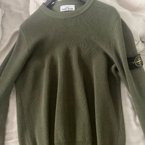 Stickad stone island tröja - Säljer en olivgrön stickad tröja från Stone Island med klassisk rund halsringning. Tröjan har lång ärm och den ikoniska Stone Island-loggan på vänster ärm. Perfekt för dig som gillar stilrena och tidlösa plagg. 