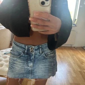 Blå jeanskjol med rå kant - Säljer en ljusblå jeanskjol med slitna detaljer och rå, fransig nederkant. Kjolen har klassiska fickor fram och bak samt dubbla knappar i midjan. Perfekt för en avslappnad stil.