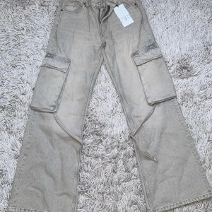 Gråa cargopants från Zara - Säljer ett par gråa cargopants från Zara med bred passform och stora fickor på sidorna. Byxorna har raka ben och detaljer längs benen. Perfekta för en avslappnad och trendig stil. 