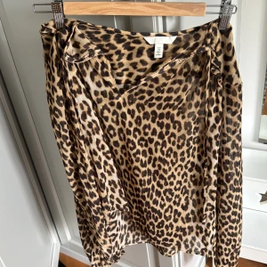 Leopardmönstrad blus från H&M - Säljer en snygg leopardmönstrad blus från H&M med v-ringning och knytband vid halsen. Blusen har långa ärmar och är tillverkad i ett lätt, transparent material. Perfekt för dig som vill sticka ut med ett djurmönster!