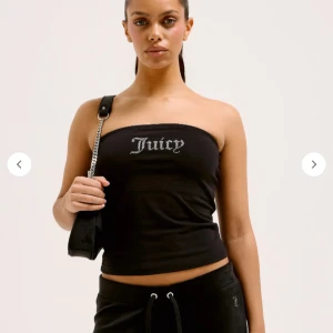 Svart tubtopp från Juicy Couture - Svart tubtopp från Juicy Couture med glittrande texten 'Juicy' framtill i strass. Enkel och stilren design utan axelband, perfekt för en trendig look.
