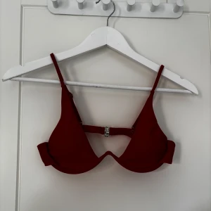 Röd bikiniöverdel med justerbara axelband - Snygg röd bikiniöverdel med justerbara axelband och metallspänne bak. Klassisk trekantsform med lätt vaddering och slät yta. Perfekt för stranden eller poolen.