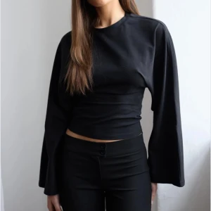 Svart långärmad topp med vida ärmar - Säljer en svart långärmad topp med rund hals och extra vida ärmar. Toppen är figurnära och har en stilren, minimalistisk design som passar perfekt till jeans eller kjol. Materialet känns mjukt och stretchigt.