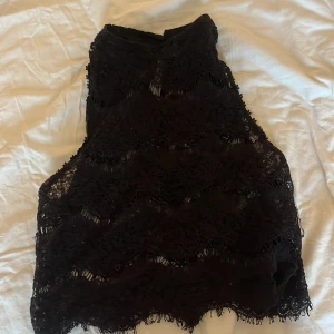 Svart spets-croppad topp från Jennyfer - Säljer en svart croppad topp från Jennyfer i spetsmaterial. Toppen är ärmlös och har hög hals med knapp i nacken. Perfekt för att skapa en trendig look med snygga spetsdetaljer och transparenta partier. Säljer pågrund av dålig användning.💖