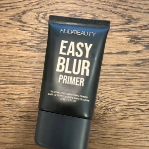 Easy Blur Primer från Huda Beauty - Halva förpackningen kvar !                                                 En svart tub med Easy Blur Primer från Huda Beauty. Primern är silikonfri och ger en jämn och slät bas för smink. Förpackningen innehåller 30 ml och har en stilren design med vit text.