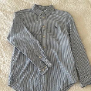 Ralph Lauren skjorta - Säljer nu denna riktigt snygga Ralph Lauren skjorta som är helt perfekt till sommaren. Den är i bra skick och är i storlek 16 (barn). Passar dig som är 160-165. Tveka inte på att höra av dig vid minsta lilla fundering!
