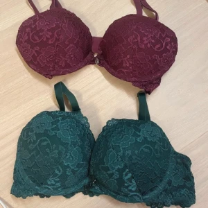 Två spets-bh:ar i vinrött och mörkgrönt - Säljer två snygga bh:ar med spetsdetaljer, en i vinrött och en i mörkgrönt. Båda har vadderade kupor och justerbara axelband. 