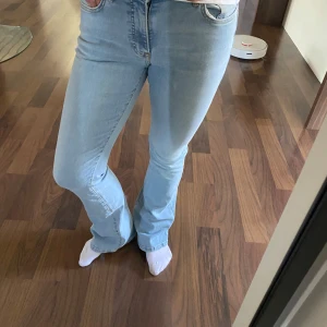 Ljusblå jeans med bootcut - Säljer ett par ljusblå jeans med klassisk femficksdesign och bootcut-ben. Jeansen har normal passform och stängs med dragkedja och knapp. Perfekta till vardags för en avslappnad stil.