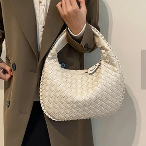 Vit flätad axelväska - Säljer en snygg vit axelväska med flätad design och dragkedja. Väskan har ett stilrent och modernt utseende, perfekt för att lyfta din outfit. Invändigt finns ett fack med dragkedja för extra förvaring. Passar dig som gillar trendiga accessoarer.