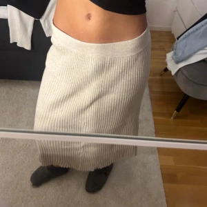Beige ribbad långkjol - Säljer en beige ribbad långkjol med hög midja. Kjolen är stickad och har en rak passform som ger en avslappnad men ändå stilren look. Perfekt att matcha med en enkel topp eller stickad tröja.