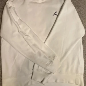 Vit sweatshirt från Jordan - Säljer en stilren vit sweatshirt från Jordan med den klassiska Jumpman-loggan broderad på bröstet. Tröjan har rund halsringning och långa ärmar. Perfekt för en sportig och avslappnad look.